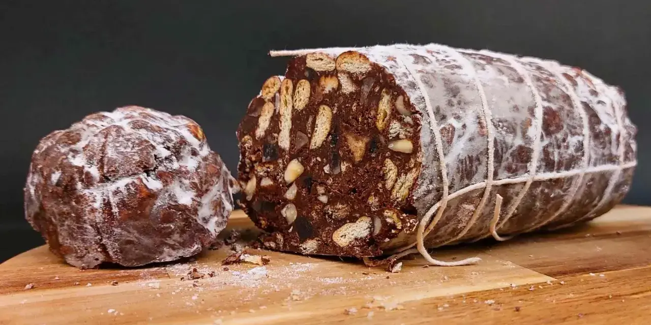 Salame al cioccolato vegano, un dolce goloso con biscotti e frutta secca, spolverato di zucchero a velo.