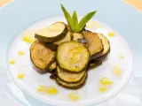 Fette di zucchine alla scapece, condite con olio e guarnite con menta fresca, su un piatto bianco.