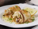 Deliziosi involtini di pesce spada ripieni, serviti su un piatto bianco con spicchio di limone e prezzemolo tritato.