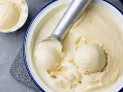 Un cucchiaio raccoglie una pallina cremosa di gelato fatto in casa, in una ciotola piena di delizia fredda.