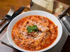 Un piatto fumante di trippa alla romana, cosparso di formaggio grattugiato e guarnito con menta fresca. Accanto, una grattugia e un pezzo di formaggio.