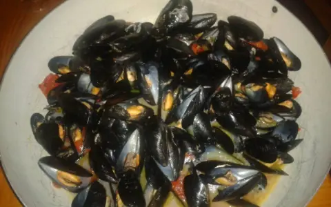 Un'abbondante impepata di cozze in un piatto largo, con pomodorini e un sughetto invitante.