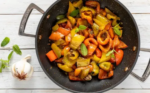 Peperoni in padella, colorati e succosi, con foglie di menta fresca e uno spicchio d'aglio.