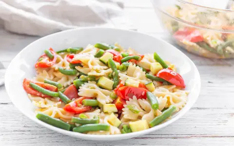 Un piatto invitante di pasta fredda vegana con farfalle, pomodorini, zucchine e fagiolini. Perfetta per un pasto leggero e gustoso.