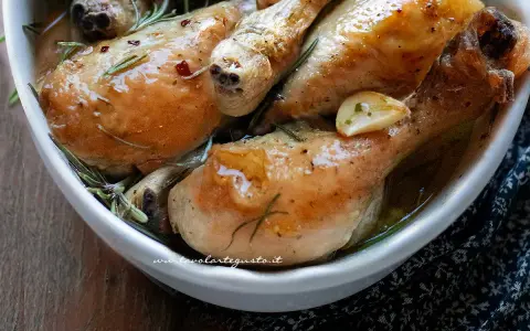 Cosce di pollo al forno succulente, dorate e profumate al rosmarino e aglio, servite in una ciotola bianca.