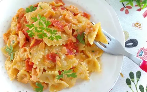 Farfalle cremose con pomodorini e salmone, guarnite con prezzemolo fresco. Un piatto invitante pronto per essere gustato.