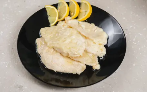 Scaloppine di pollo al limone, un piatto classico e saporito, servite su un piatto nero con spicchi di limone fresco.