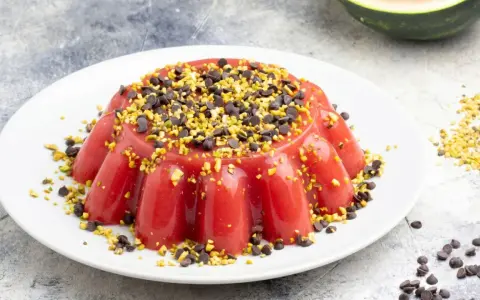 Delizioso gelo di melone rosso, guarnito con gocce di cioccolato e pistacchi tritati, su un piatto bianco.