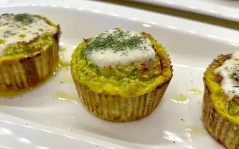 Tre tortini di zucchine dorati, guarniti con formaggio fuso e aneto, serviti su un piatto bianco.