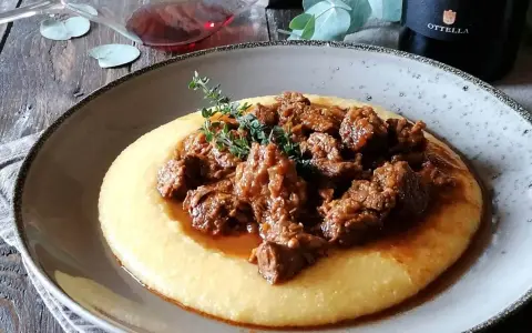 Un piatto di gulash con polenta fumante, guarnito con rametti di timo fresco. Un classico confortante, perfetto per una cena speciale.