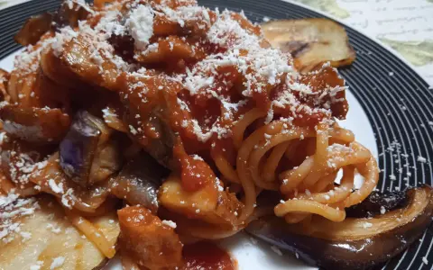 Un piatto invitante di pasta alla norma con melanzane fritte, sugo di pomodoro e ricotta salata grattugiata.