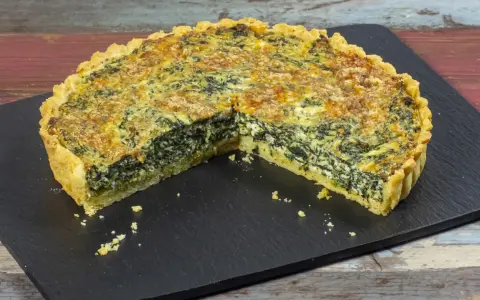 Una fetta di torta salata ricotta e spinaci, con crosta dorata e ripieno cremoso, su una lavagna scura.