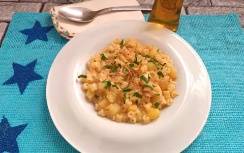Un piatto di pasta patate e provola fumante, guarnito con prezzemolo fresco e un pizzico di peperoncino, pronto per essere gustato.