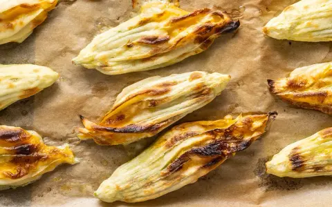 Fiori di zucca in pastella dorati e croccanti, appena sfornati su carta da forno.