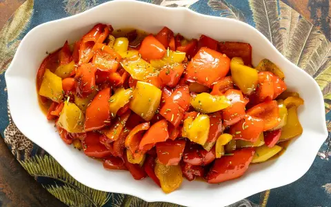 Peperoni in umido, colorati e succulenti, conditi con erbe aromatiche, serviti in una ciotola bianca su un tovagliolo decorato.