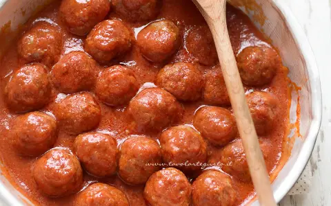 Succulente polpette di carne in un sugo rosso, pronte per essere gustate. Un cucchiaio di legno attende di servirle.