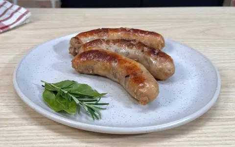 Tre salsicce dorate in padella, servite su un piatto con rosmarino e alloro.