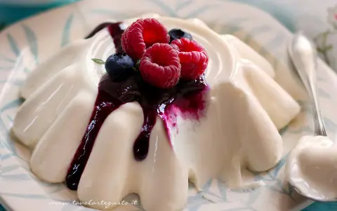Deliziosa panna cotta con frutti di bosco e salsa ai mirtilli, servita su un piatto decorato.