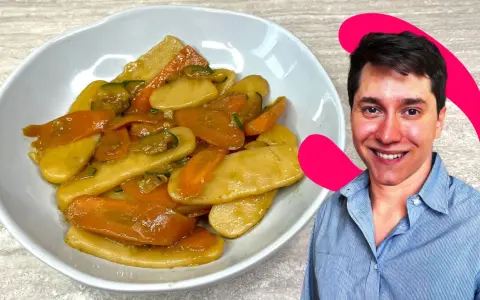 Un uomo sorride accanto a un piatto di gnocchi di riso con carote e zucchine.