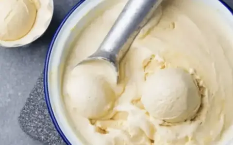 Un cucchiaio raccoglie una pallina cremosa di gelato fatto in casa, in una ciotola piena di delizia fredda.