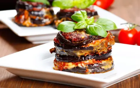 Parmigiana di melanzane, un classico della cucina italiana, servita su un piatto bianco con basilico fresco.
