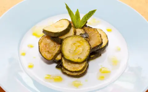 Fette di zucchine alla scapece, condite con olio e guarnite con menta fresca, su un piatto bianco.