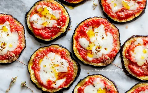 Pizzette di melanzane al forno, con pomodoro, mozzarella filante e un filo d'olio. Un antipasto sfizioso e leggero.