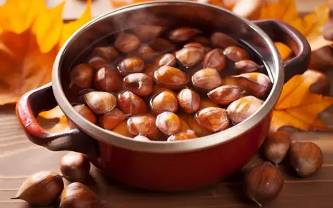 Castagne bollite con buccia in una pentola rossa, circondate da foglie autunnali.