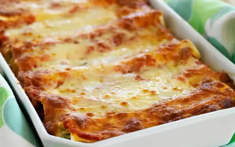 Cannelloni con ricotta appena sfornati, dorati e filanti, in una teglia bianca.