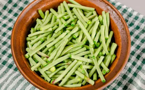 Fagiolini freschi, tagliati e pronti per essere cucinati in umido, in una ciotola di terracotta su una tovaglia a quadri verdi.