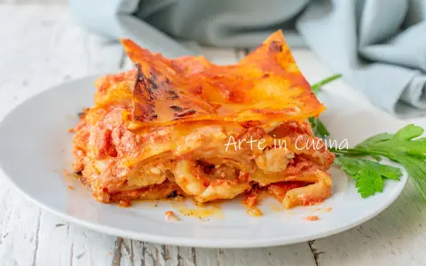 Una fetta di lasagna di mare napoletana, ricca e saporita, servita su un piatto bianco con un rametto di prezzemolo.