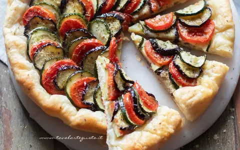 Una deliziosa torta salata estiva con zucchine, melanzane e pomodori disposti a raggiera su una base croccante.