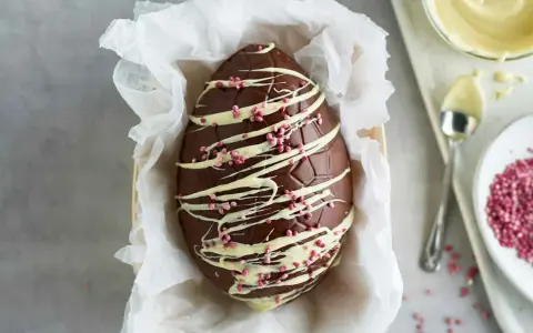 Un magnifico uovo di Pasqua fatto in casa, decorato con cioccolato bianco e granella rosa.