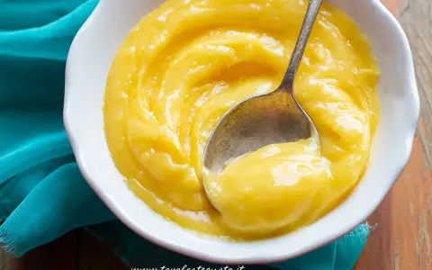 Una ciotola bianca piena di vellutata crema al limone, con un cucchiaino che ne raccoglie una porzione.