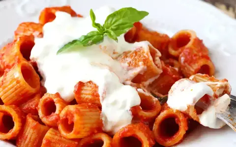 Rigatoni al sugo con abbondante stracciatella cremosa e una fogliolina di basilico fresco.