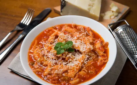 Un piatto fumante di trippa alla romana, cosparso di formaggio grattugiato e guarnito con menta fresca. Accanto, una grattugia e un pezzo di formaggio.
