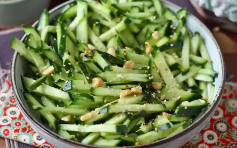 Una ciotola piena di fresca insalata di cetrioli tagliati a julienne, condita con semi di sesamo e arachidi croccanti.
