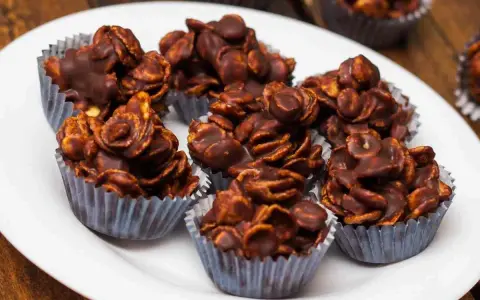Deliziosi biscotti corn flakes e cioccolato, croccanti e golosi, serviti in pirottini argentati su un piatto bianco.