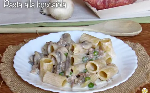 Piatto di pasta alla boscaiola con funghi, piselli e salsiccia, servita su un piatto bianco bordato.
