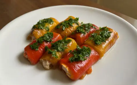 Involtini di peperoni alla siciliana, ripieni e guarniti con prezzemolo fresco, su un piatto bianco.