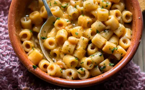 Un piatto invitante di pasta e fagioli estiva, condita con erbe fresche, servita in una ciotola di terracotta.