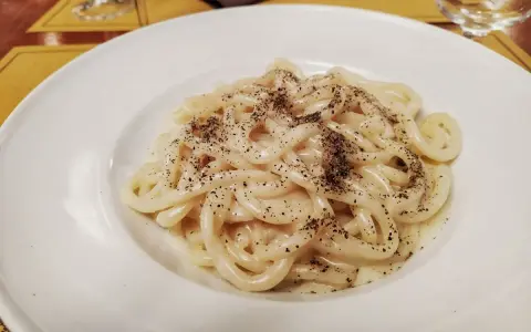 Pici cacio e pepe, un classico piatto romano, servito in un piatto bianco, con abbondante pepe nero macinato.