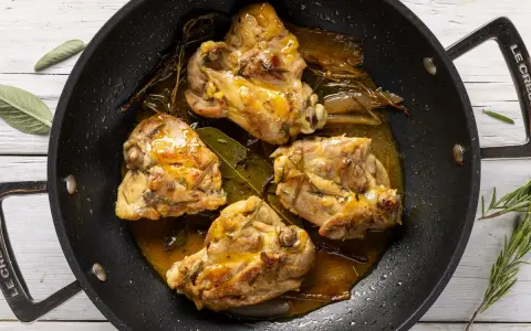 Cosce di pollo in padella, dorate e succulente, con erbe aromatiche e un sughetto invitante.