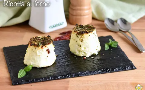 Due tortini di ricotta al forno, dorati e profumati, serviti su ardesia con basilico e peperoncino.