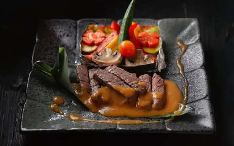 Straccetti di manzo succulenti su un piatto scuro, accompagnati da verdure miste e una salsa cremosa.