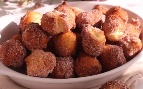 Un piatto colmo di castagnole ricetta della nonna, dorate e cosparse di zucchero. Un dolce che sa di casa e tradizione.