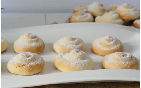 Biscotti a spirale cosparsi di zucchero a velo, perfetti con una tazza di caffè o tè, magari preparati con un tocco di latte condensato.