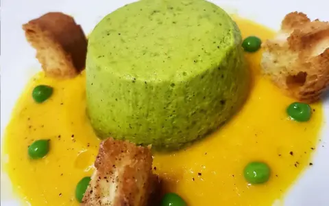 Sformato di piselli verde brillante su crema gialla, guarnito con piselli freschi e crostini dorati.