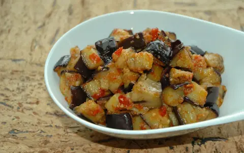 Melanzane al microonde, tagliate a cubetti e condite con pomodoro e spezie, servite in una ciotola bianca.
