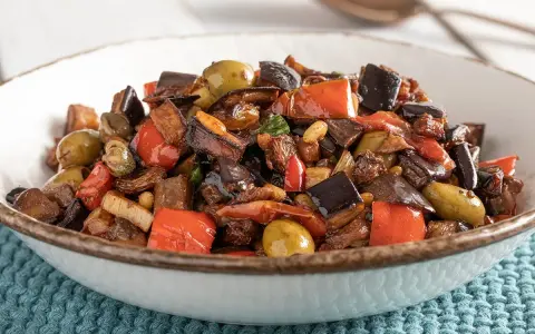 Caponata ricetta: melanzane, peperoni, olive e capperi in un piatto invitante.